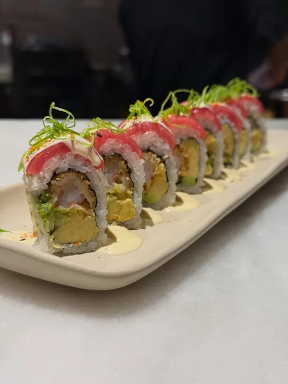 A row of maki topped with tuna and green shoots