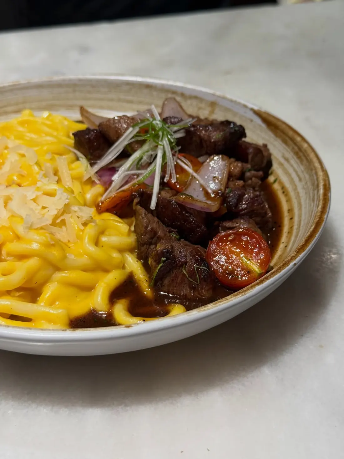 Yellow udon in huancaína sauce next to lomo saltado with tomato and onion
