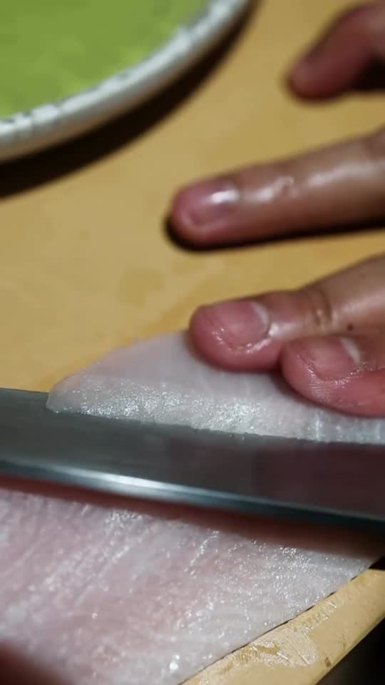 Unas manos cortan una lámina de pescado blanco con un cuchillo sobre la tabla
