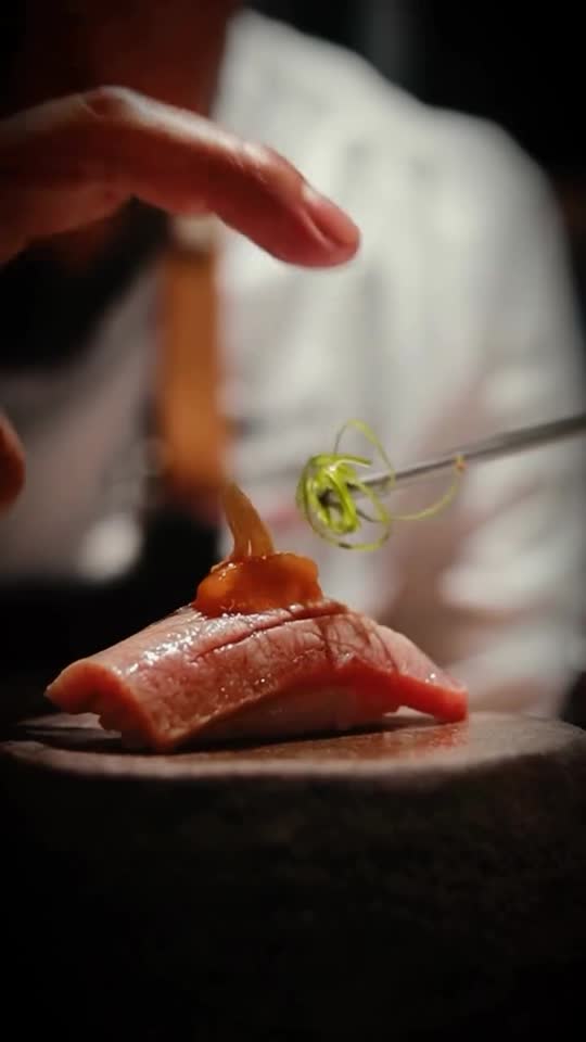 Unas pinzas colocan el adorno sobre un nigiri de atún, en su piedra volcánica