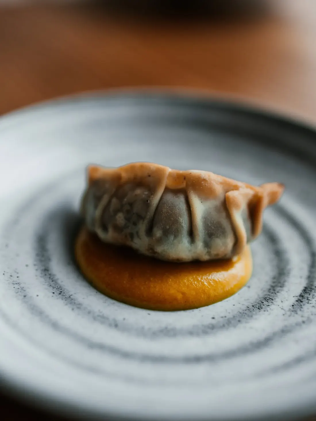 A golden gyoza on yellow sauce on a grey plate