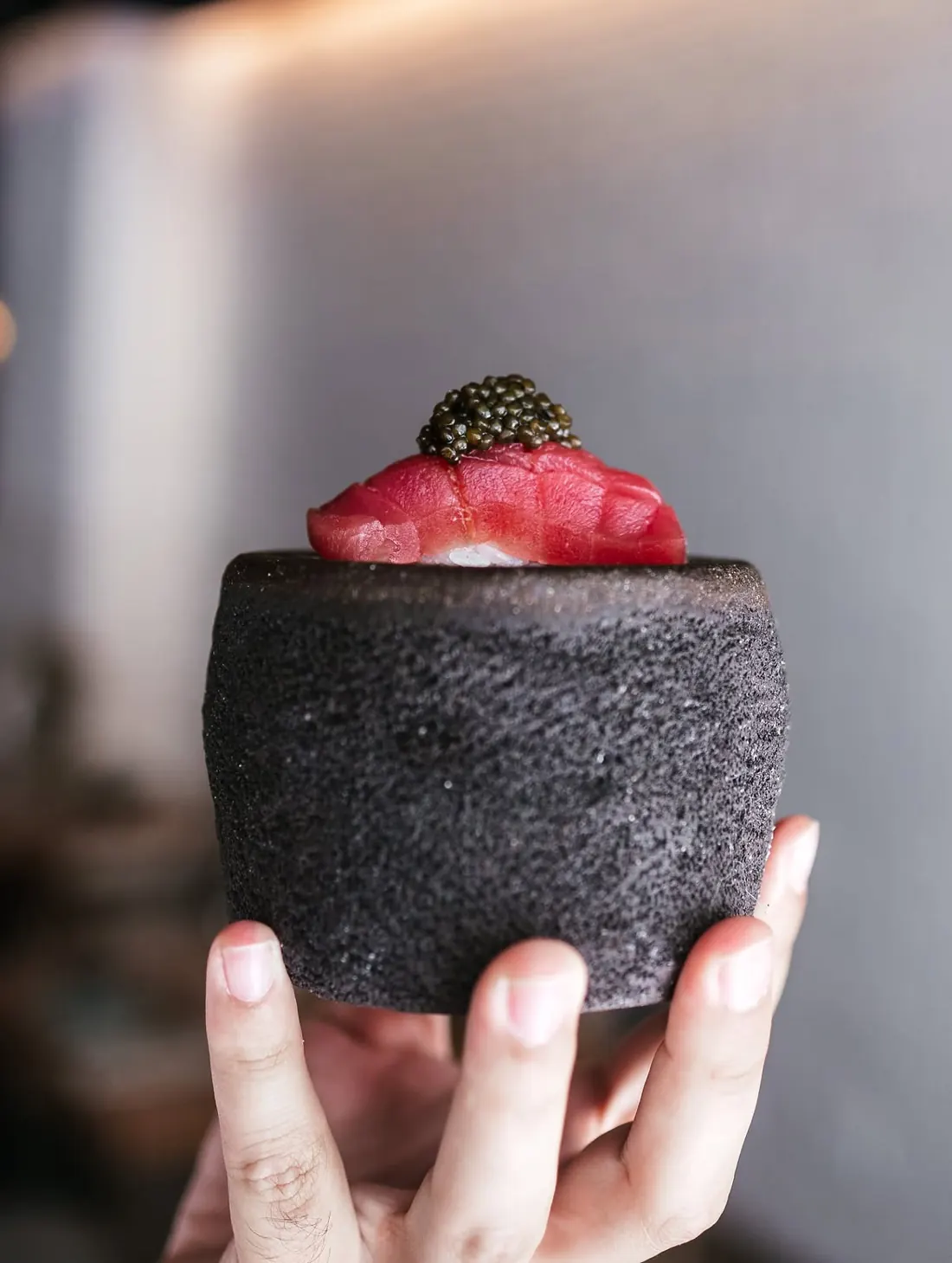 A hand holding the volcanic stone with a tuna nigiri topped with caviar