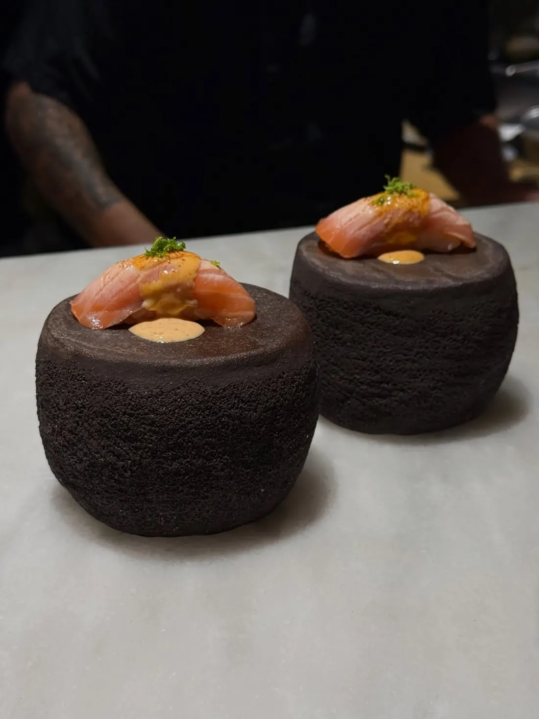 Dos nigiris de salmón flameado sobre piedras volcánicas, en la barra