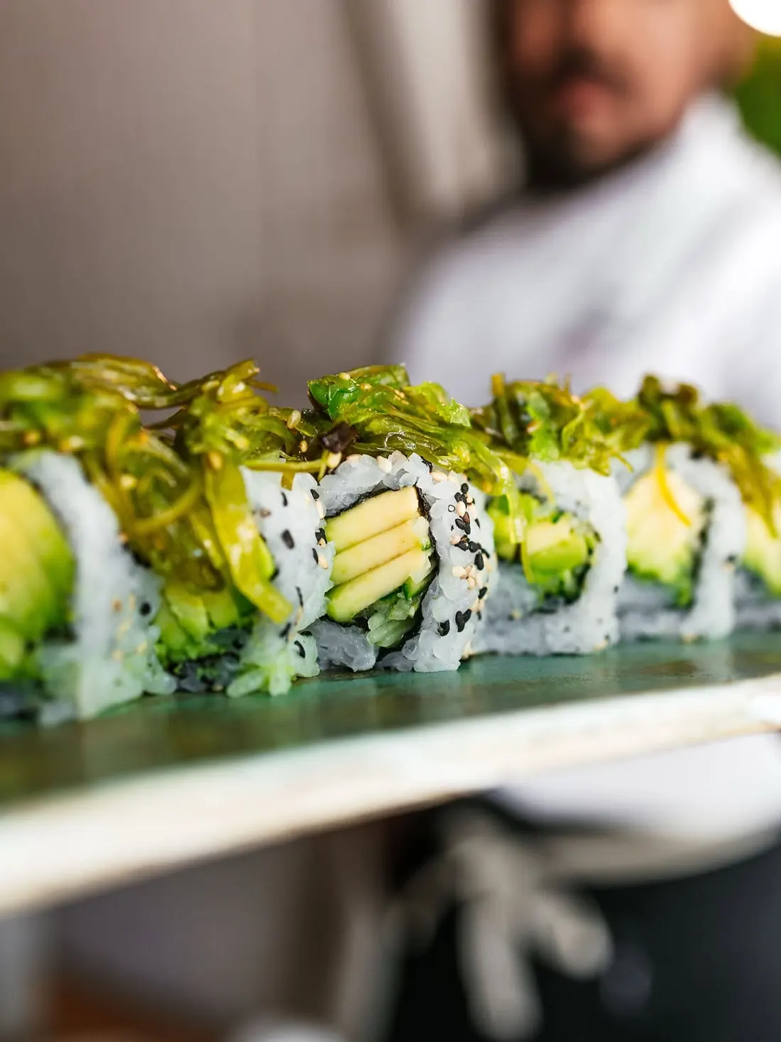 El chef enseña una fila de rolls de aguacate cubiertos de alga wakame