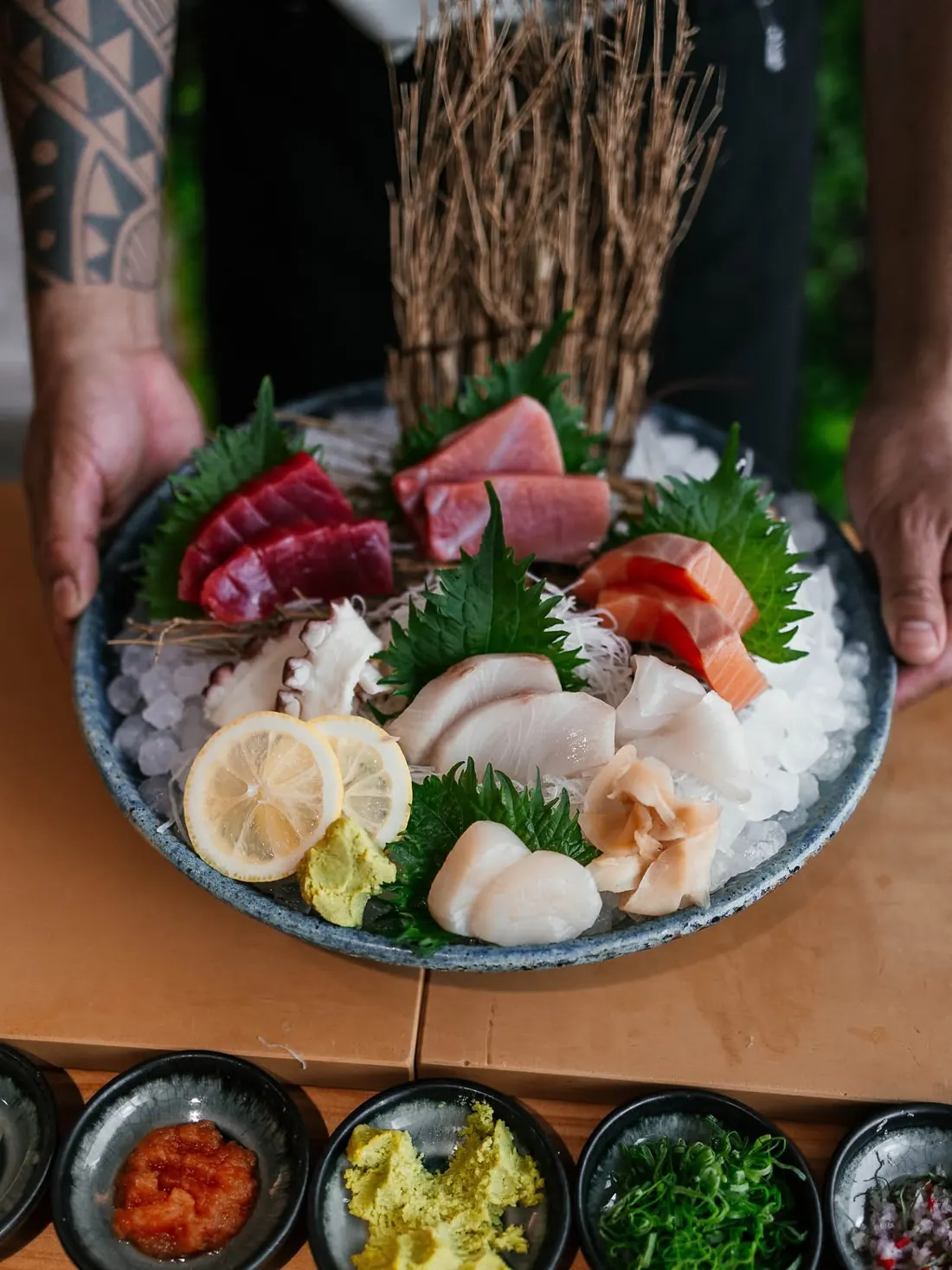 A cook holds a platter of assorted sashimi on crushed ice, with lemon and green leaves