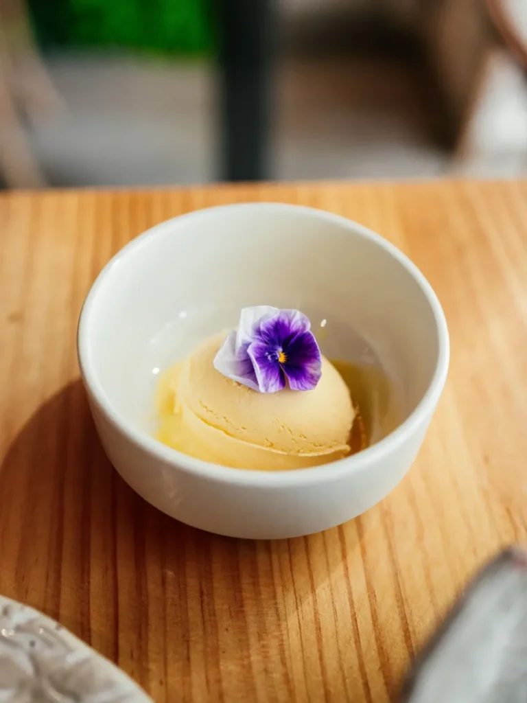 Helado amarillo con una flor comestible en un cuenco blanco en Lima Nikkei